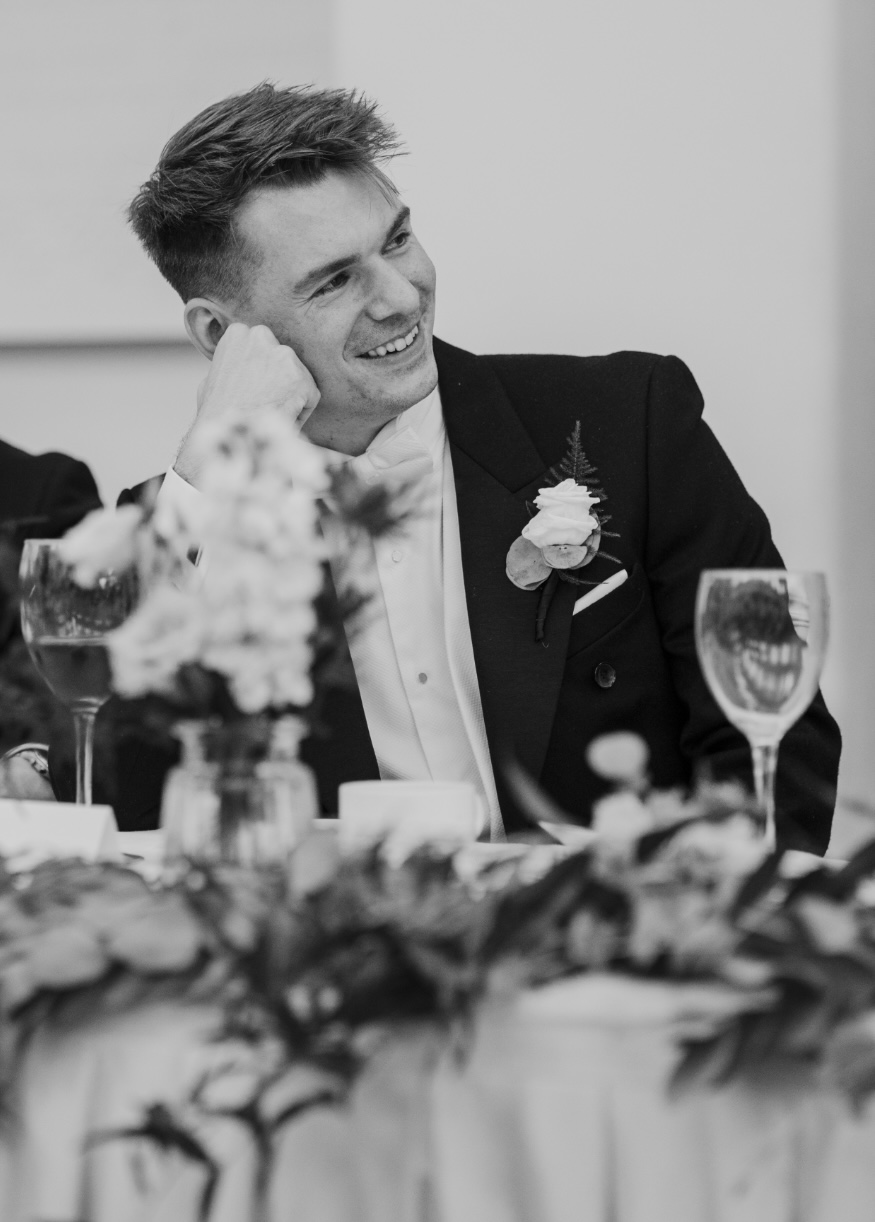 A close-up of an individual's hand seated at a table, wearing a black suit jacket, as they apply a brown wax seal to a doc...